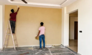Construction workers applying textured wall finish on a ladder during interior execution, project management